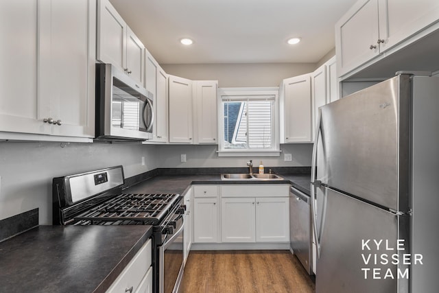 135 Houseman Ave NE, Grand Rapids, MI 49503 - kitchen featuring a sink, wood finished floors, stainless steel appliances, dark countertops, and white cabinets