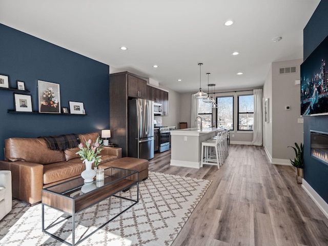living room with recessed lighting, baseboards, visible vents, a glass covered fireplace, and wood finished floors
