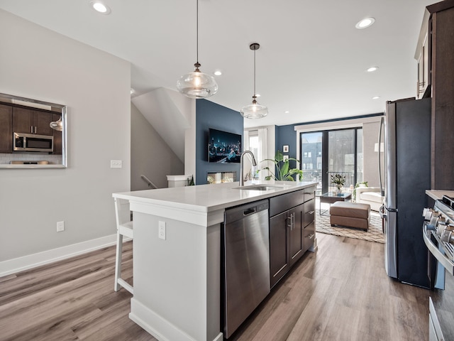 kitchen featuring a sink, an island with sink, light wood finished floors, dark brown cabinets, and appliances with stainless steel finishes
