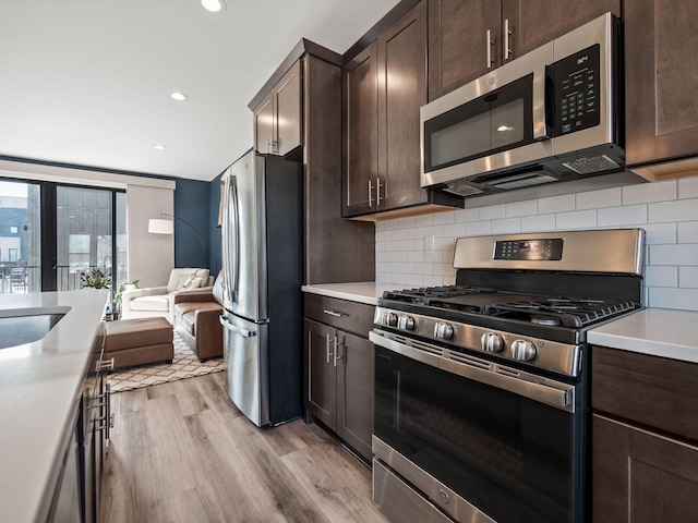 kitchen featuring open floor plan, light countertops, light wood-type flooring, stainless steel appliances, and dark brown cabinets