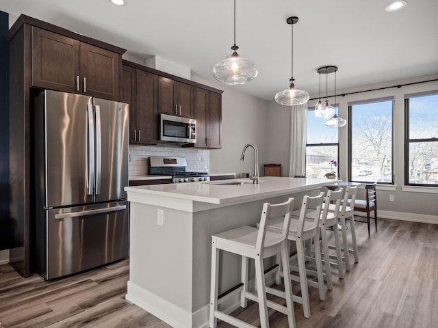 kitchen featuring dark brown cabinetry, backsplash, a sink, stainless steel appliances, and a kitchen island with sink