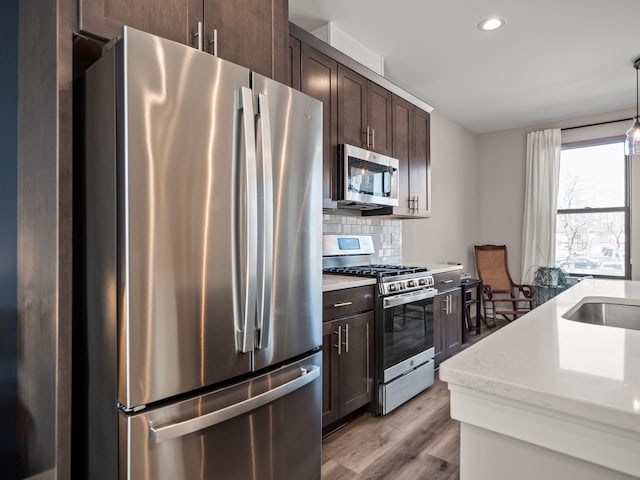 kitchen featuring tasteful backsplash, stainless steel appliances, hanging light fixtures, light wood finished floors, and dark brown cabinetry