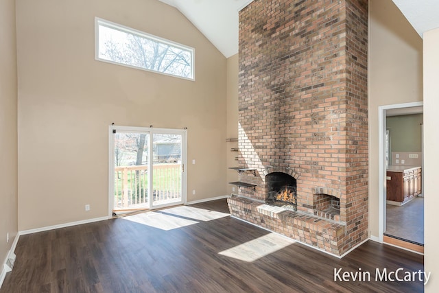 unfurnished living room with baseboards, high vaulted ceiling, wood finished floors, and a brick fireplace