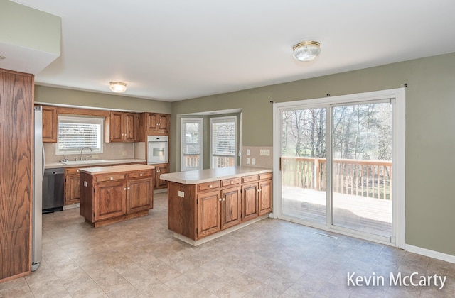 kitchen featuring light countertops, a peninsula, oven, stainless steel dishwasher, and brown cabinetry