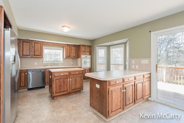 kitchen featuring light countertops, a peninsula, stainless steel appliances, a sink, and brown cabinetry