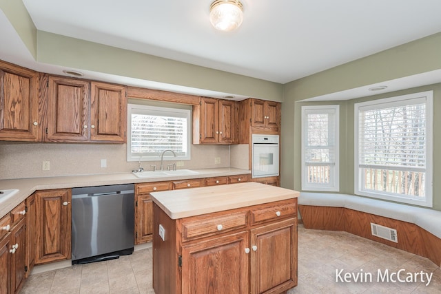 kitchen with a sink, white oven, brown cabinets, and stainless steel dishwasher
