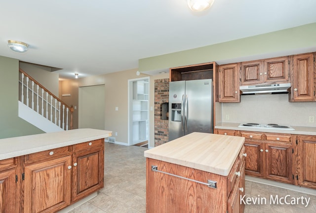 kitchen featuring stainless steel fridge, a center island, under cabinet range hood, white electric cooktop, and brown cabinets