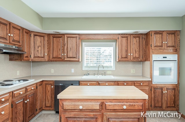 kitchen with light countertops, a sink, brown cabinets, under cabinet range hood, and white appliances