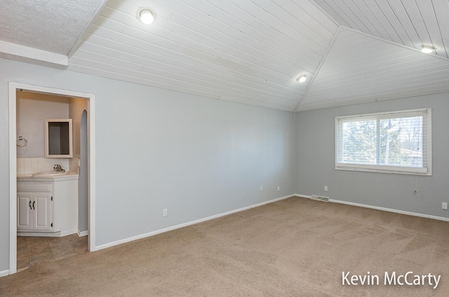 unfurnished bedroom featuring vaulted ceiling, light colored carpet, baseboards, a sink, and visible vents