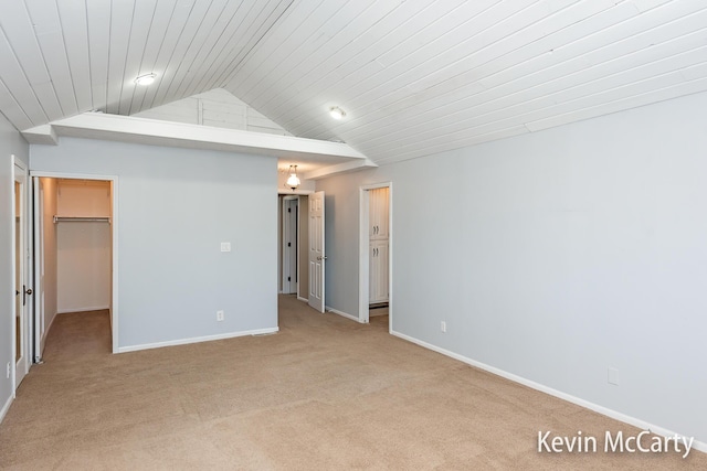 unfurnished bedroom featuring light colored carpet, lofted ceiling, baseboards, and a spacious closet