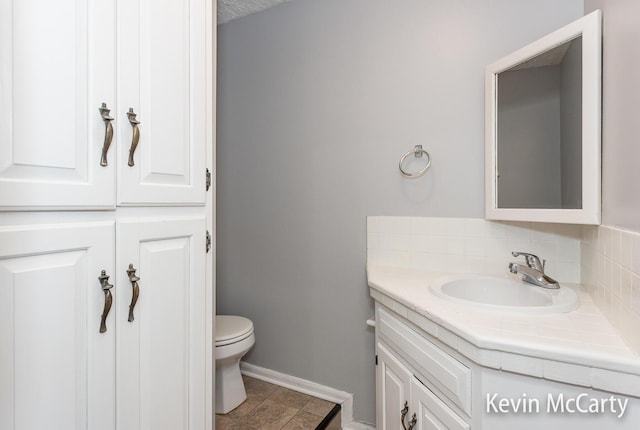 bathroom featuring toilet, vanity, tasteful backsplash, and baseboards