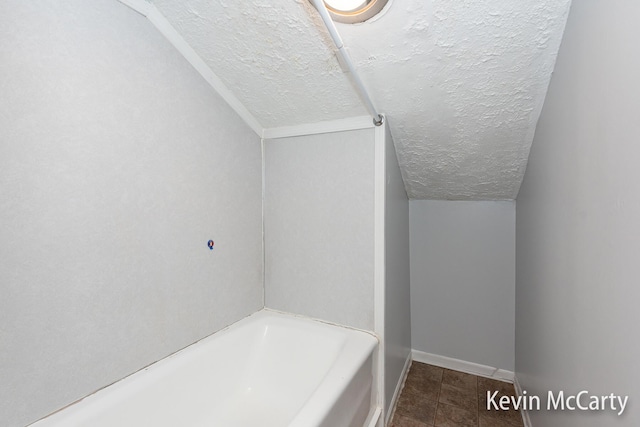 bathroom with baseboards, a textured ceiling, a washtub, and vaulted ceiling