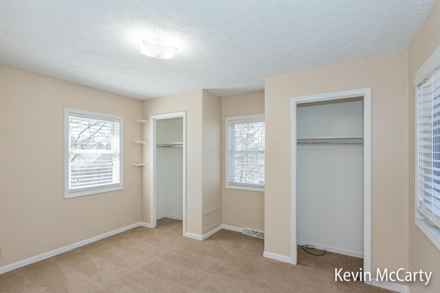 unfurnished bedroom with carpet flooring, a textured ceiling, multiple closets, baseboards, and visible vents