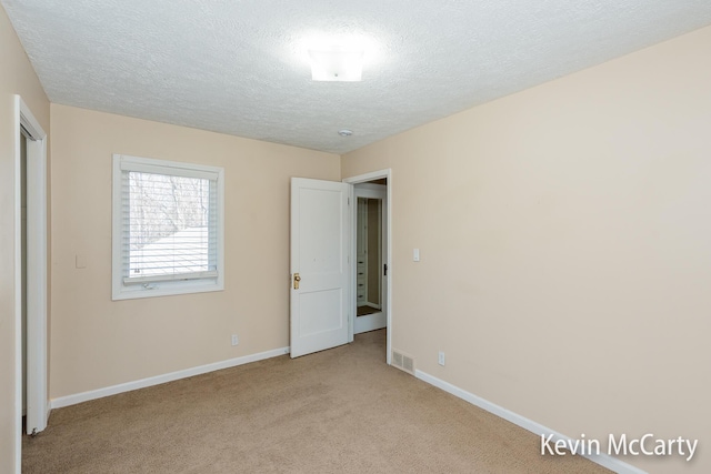 unfurnished bedroom featuring baseboards, a textured ceiling, visible vents, and light carpet