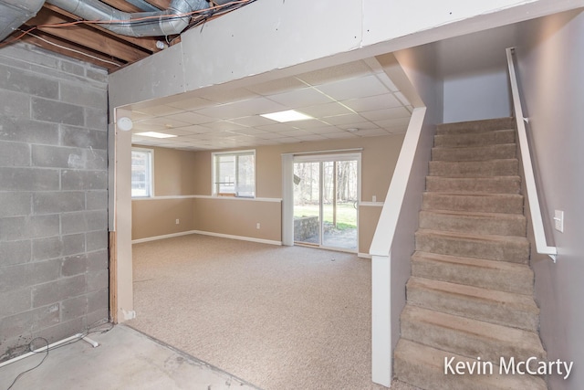 basement featuring a drop ceiling, concrete block wall, and stairway
