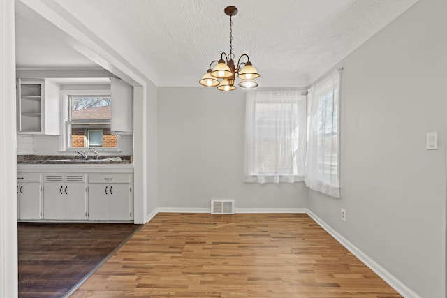 unfurnished dining area featuring light wood-type flooring, an inviting chandelier, visible vents, and a textured ceiling