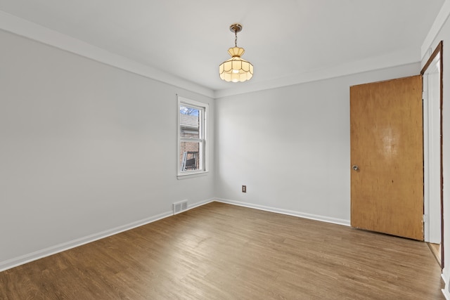 unfurnished room with baseboards, wood finished floors, and visible vents