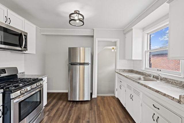 kitchen featuring dark wood finished floors, stainless steel appliances, a sink, baseboards, and white cabinetry