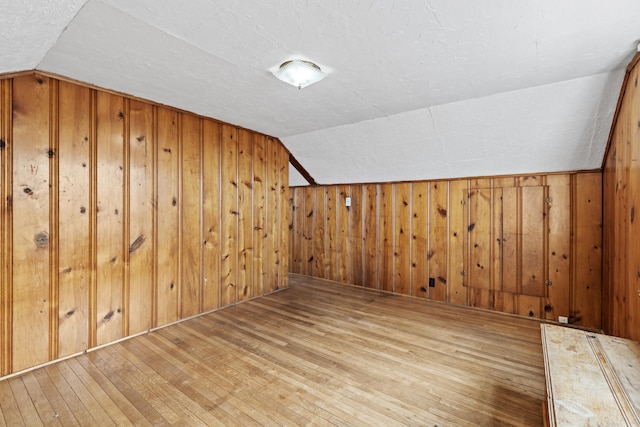 additional living space with vaulted ceiling, hardwood / wood-style floors, and wood walls