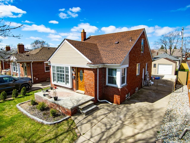 rear view of house with a detached garage, concrete driveway, a chimney, an outdoor structure, and brick siding