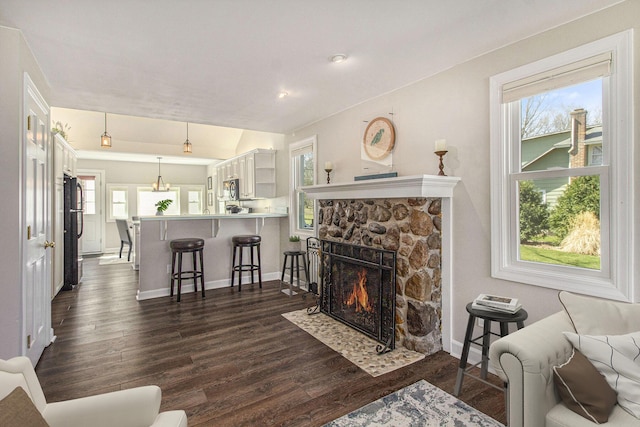 living room featuring a stone fireplace, baseboards, a healthy amount of sunlight, and dark wood finished floors