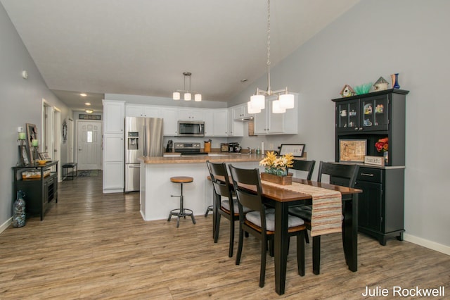 dining space featuring baseboards, vaulted ceiling, light wood-style flooring, and a notable chandelier