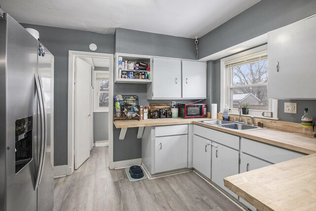kitchen featuring light wood finished floors, a sink, white cabinets, and stainless steel fridge