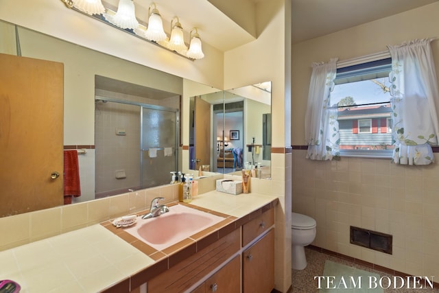 bathroom with vanity, tile walls, a shower stall, visible vents, and wainscoting