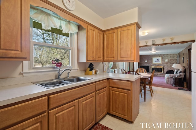 kitchen featuring light countertops, a sink, a peninsula, and a fireplace