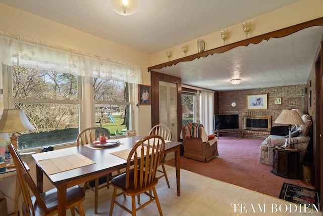dining space with light colored carpet, a fireplace, brick wall, and a healthy amount of sunlight