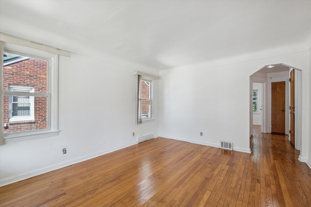empty room with arched walkways, hardwood / wood-style floors, visible vents, and baseboards
