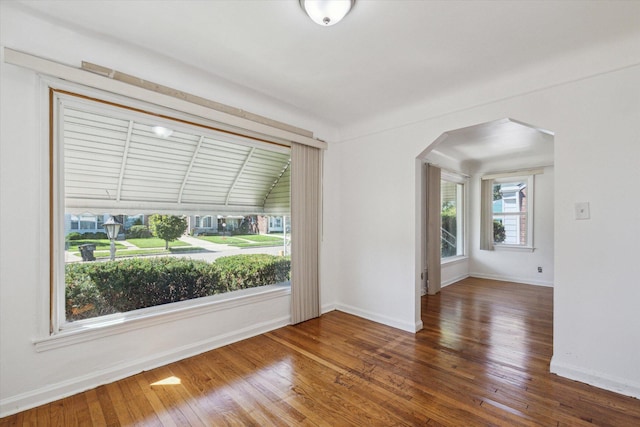 unfurnished room with arched walkways, wood finished floors, and baseboards