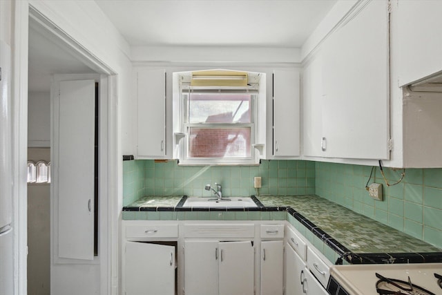 kitchen with a sink, white gas stove, backsplash, white cabinetry, and tile countertops