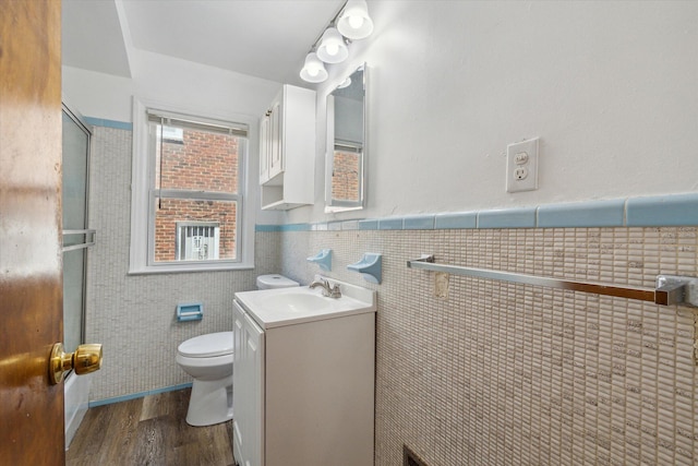 full bathroom featuring a shower with shower door, toilet, tile walls, wood finished floors, and vanity