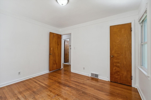 empty room featuring baseboards, wood finished floors, and visible vents