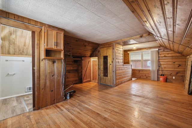bonus room with lofted ceiling, light wood-style flooring, visible vents, and wood walls