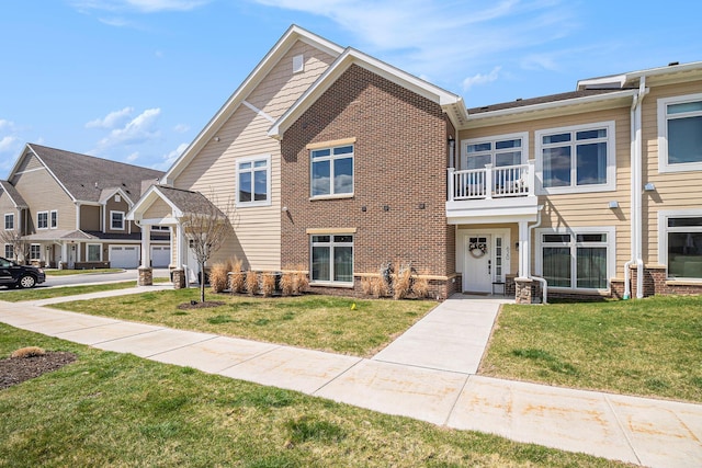 multi unit property featuring a balcony, a front yard, and brick siding