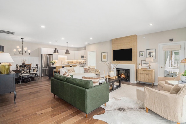 living area featuring a large fireplace, visible vents, recessed lighting, wood finished floors, and a notable chandelier