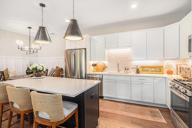 kitchen with white cabinetry, a chandelier, wood finished floors, a sink, and stainless steel appliances