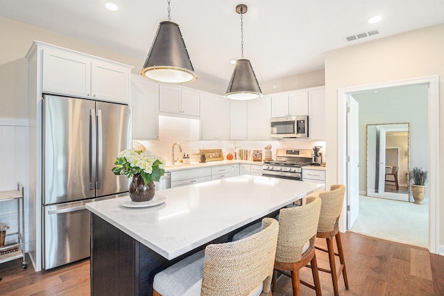 kitchen featuring visible vents, appliances with stainless steel finishes, a kitchen bar, and dark wood-style floors