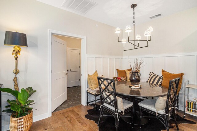 dining area featuring wood finished floors, an inviting chandelier, visible vents, and a wainscoted wall