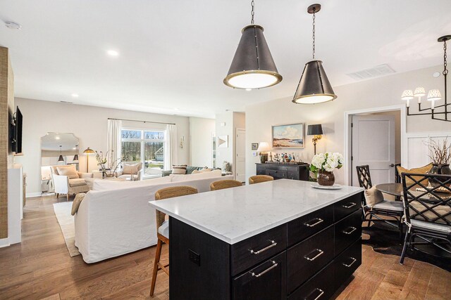 kitchen with visible vents, a kitchen island, a breakfast bar, wood finished floors, and dark cabinetry