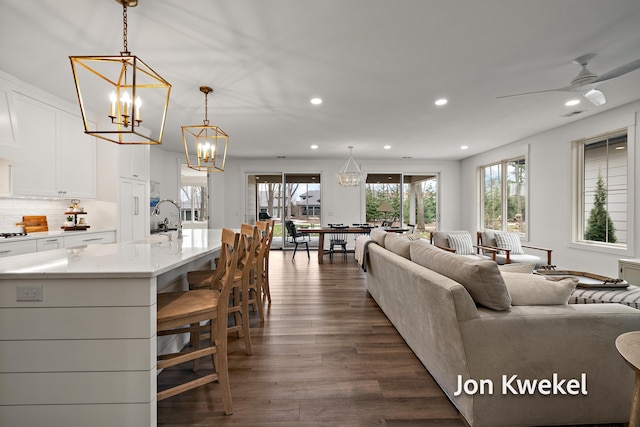 living room featuring ceiling fan with notable chandelier, dark wood finished floors, and recessed lighting