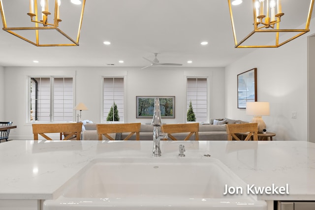 kitchen with open floor plan, light stone counters, a sink, and recessed lighting