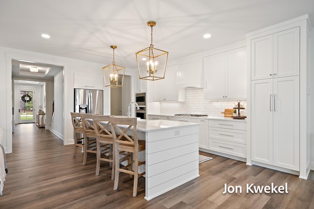 kitchen featuring white cabinets, custom exhaust hood, a kitchen island with sink, light countertops, and decorative backsplash
