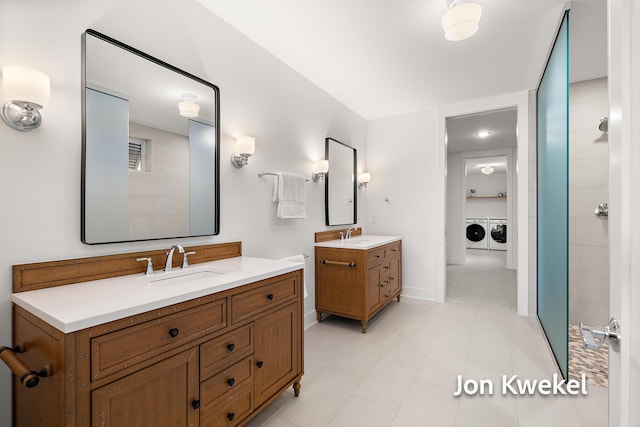 full bathroom with two vanities, baseboards, a sink, independent washer and dryer, and a tile shower