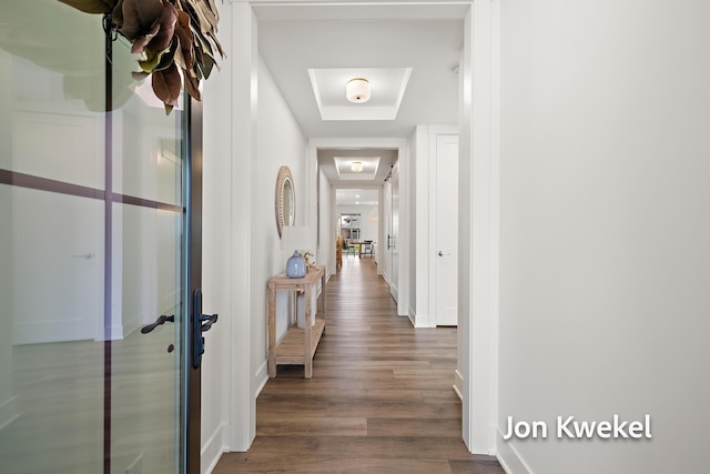 corridor featuring a tray ceiling, baseboards, and wood finished floors