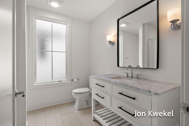 full bath featuring a wealth of natural light, vanity, baseboards, and toilet