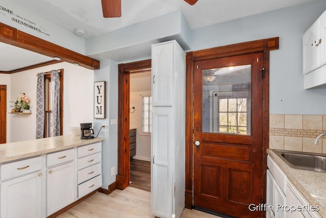 kitchen featuring white cabinetry, light wood finished floors, a sink, and a ceiling fan
