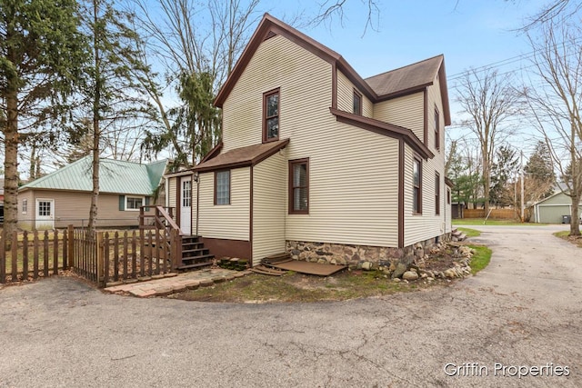 view of property exterior featuring aphalt driveway, fence, and a shingled roof